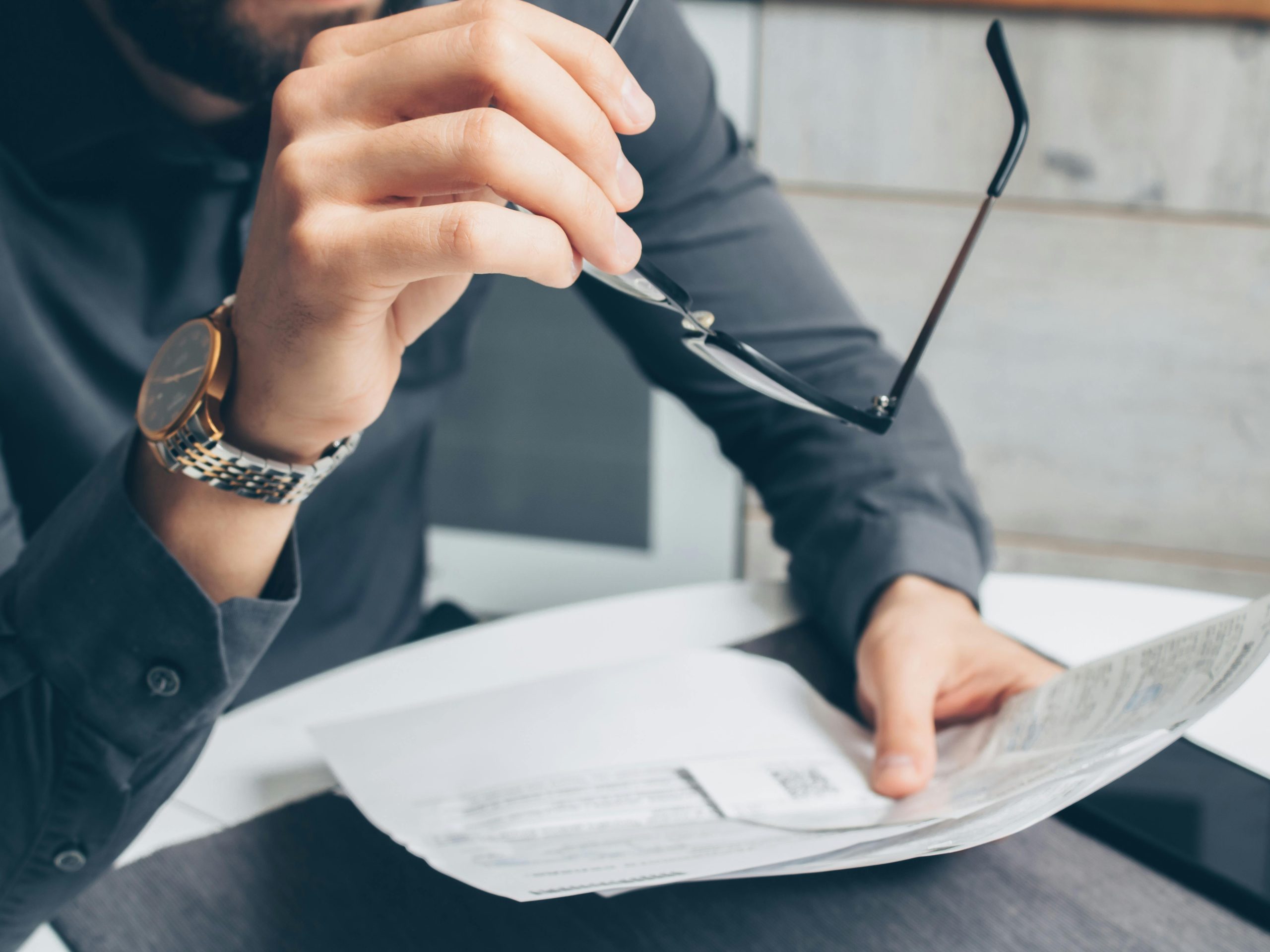 Close-up of a person holding glasses and reviewing financial documents, symbolizing financial reflection and decision-making.