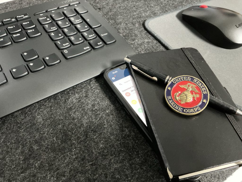 Pocket notebook with a United States Marine Corps challenge coin and a smartphone running the FitBudget app on a desk